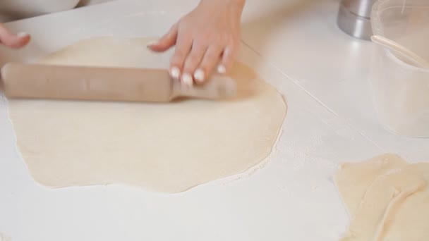 Une boulangère déploie une pâte avec un rouleau à pâtisserie sur le fond des ingrédients sur une table en bois et de la farine. Gros plan . — Video