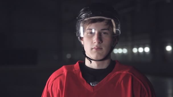 Jogador de hóquei bonito. Sorrindo para a câmera na arena escura, feche o retrato de defensor ou jogador canadense avançado — Vídeo de Stock