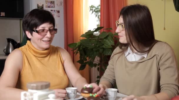 Mãe e filha nova com óculos beber chá ou café na cozinha e comer bolos, falar, rir — Vídeo de Stock
