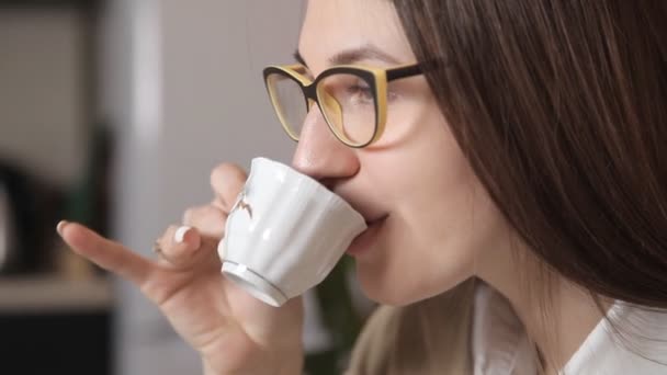 De cerca. Hermosa chica con gafas de beber café con una pequeña taza y hablar con alguien — Vídeos de Stock