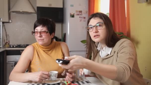 Μαμά και κόρη με γυαλιά παρακολουθώντας ειδήσεις στην τηλεόραση και να πιείτε καφέ ή καφέ. Κάτι συμβαίνει, και καλεί την κόρη — Αρχείο Βίντεο