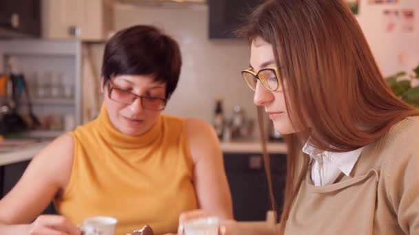 Mãe e filha com óculos assistindo as notícias na TV e beber chá ou café. Algo acontece e a filha liga. — Vídeo de Stock