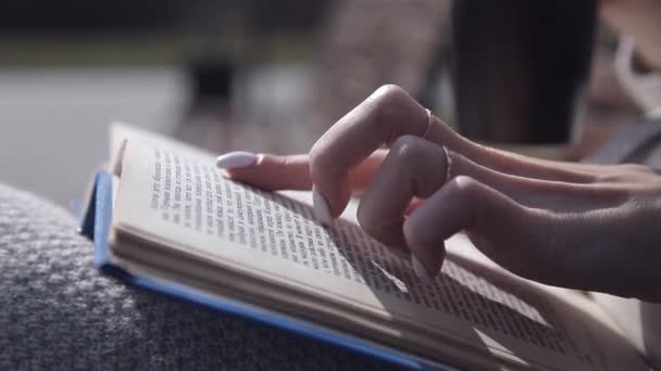Close up. beautiful female fingers watching the book. Другая рука держит термическую кружку — стоковое видео