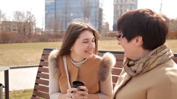 Mother and daughter are sitting in spring Park for coffee break after shopping, happy family and people concept — Stock Video