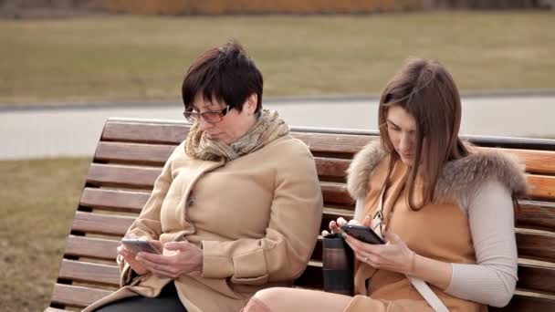 Mère et fille assises dans le parc communiquent et utilisent un téléphone portable. Nature, relations — Video