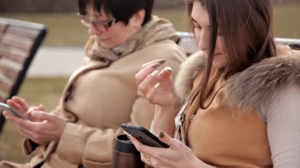 Matka a dcera, kteří sedí v parku, komunikují a používají mobilní telefon. Příroda, vztahy — Stock video