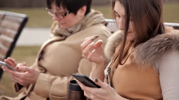 Madre e figlia sedute nel parco comunicano e usano un telefono cellulare. Natura, relazioni — Video Stock