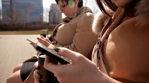 Mãe e filha se sentam no parque em um banco e usam telefones celulares — Vídeo de Stock