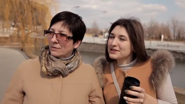 Une belle mère mature et sa fille adulte parlent, sourient, marchent ensemble dans la rue de la ville.différentes générations, concept de famille — Video