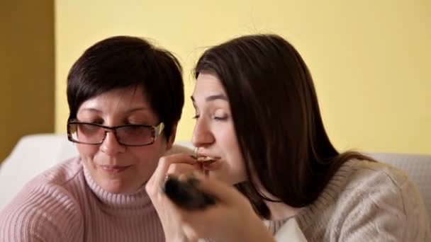 Mama i jej córka jedzą żetony podczas picia TV i pić Cola. Przytulna atmosfera w domu — Wideo stockowe