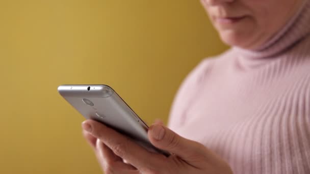 Una mujer con gafas escribiendo un mensaje en su nuevo smartphone mientras está sentada en el sofá con una almohada blanca en casa — Vídeo de stock