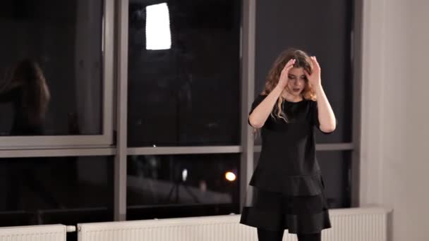Een jong meisje in een zwarte jurk repetierende dans, de dame is bezig met moderne stijl. Energie, hal, venster, dans — Stockvideo