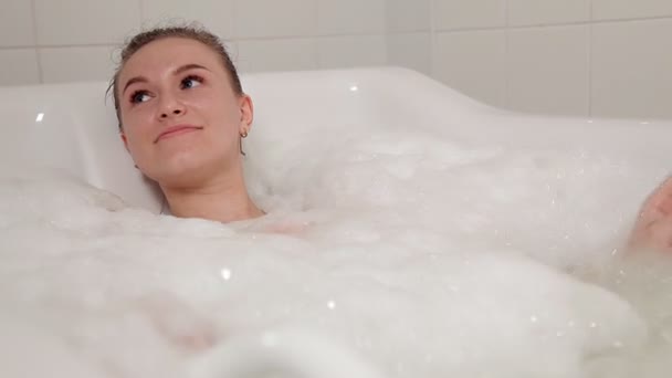 Een jong meisje in een badpak besteedt tijd in de Spa, liggend in de badkamer met hydromassage — Stockvideo