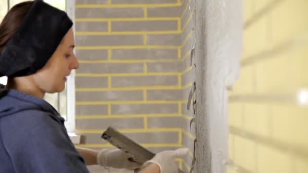 Jonge meid stopverf, plak op de muur, en richt dan de stopverf op de muur met zijn hand. Reparatie, gladde muren — Stockvideo