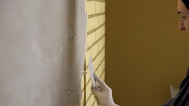 Reparatur zu Hause. Das Mädchen streicht den Putz mit einem großen Metallspachtel auf die Wand, um den Putz an der Wand auszurichten. Reparaturarbeiten — Stockvideo