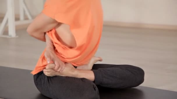 Hombre atlético joven sentado en postura de yoga en estera azul en el gimnasio con espejos. Yoga, deporte, relajación, flexibilidad — Vídeos de Stock