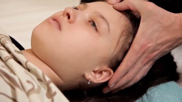 Närbild av en liten flicka vid en osteopatisk terapi session. Terapeuten manipulerar barnets huvud. Massage på spaet — Stockvideo