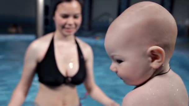 Young mother teaches baby to swim in the pool. She sits by the water, then helps him dive. Cute baby — 비디오