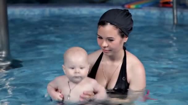 Uma criança pequena aprende a nadar na piscina com sua mãe.Piscina com água azul. Educação, cuidados, saúde — Vídeo de Stock