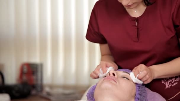 De schoonheidsspecialiste reinigt het gezicht van een mooi meisje uit de overblijfselen van het masker met behulp van natte doekjes. Cosmetische procedure voor de verjonging van de vrouwelijke huid in de schoonheidssalon — Stockvideo