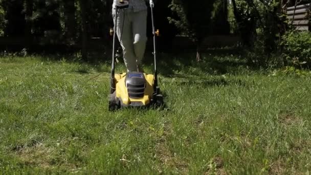 Flickan klipper en ojämn gräsmatta med gula gräsklipparen barfota — Stockvideo