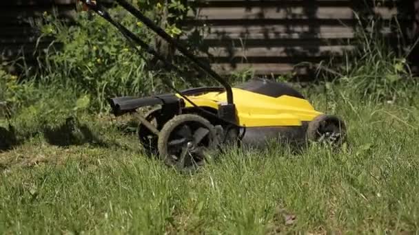 Девушка стрижет неровный газон босиком с желтой газонокосилкой. close up — стоковое видео
