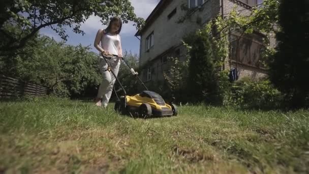 A menina está cortando um gramado desigual com cortador de grama amarelo descalço — Vídeo de Stock