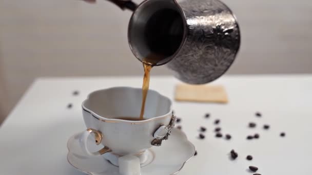 一位女士把热的芳香咖啡倒进杯中, 放在一张白色的桌子上, 咖啡豆散落在桌子上。美味的咖啡, 早晨, 觉醒 — 图库视频影像