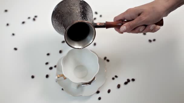 Kobieta nalewanie gorącej aromatycznej kawy do filiżanki przy białym stole, na którym ziarna kawy są rozproszone. Pyszne kawy, rano, przebudzenie — Wideo stockowe