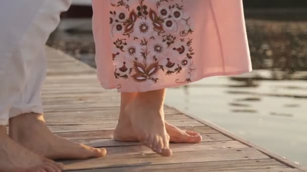 Verliebte auf einer Holzbrücke bei Sonnenuntergang. Nahaufnahme von nackten Füßen. Wasser im Hintergrund — Stockvideo