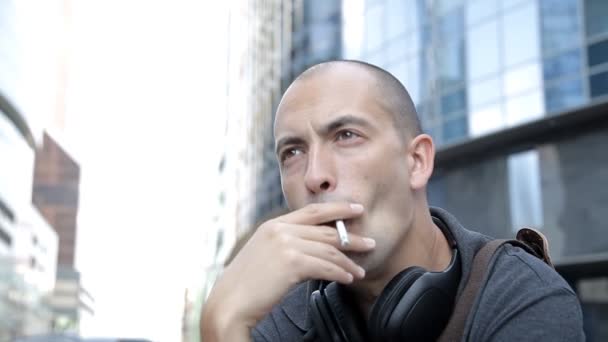 Un hombre con auriculares Fumar en el centro de la ciudad en el fondo de los rascacielos — Vídeos de Stock