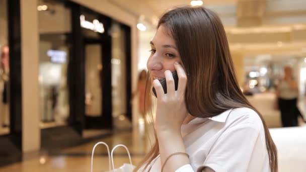 Het meisje gebruikt de telefoon in het winkelcentrum zittend op een bankje — Stockvideo