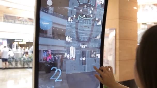 La ragazza utilizza un tavolo di informazioni ad alta tecnologia, lo schermo nel centro commerciale considerando lo schema dei negozi — Video Stock