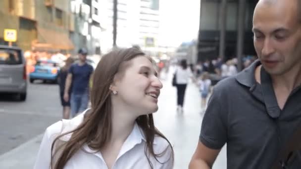 Друзья, мужчина и женщина, идущие по оживленной улице в центре города и разговаривающие, улыбающиеся — стоковое видео