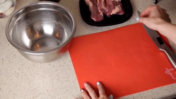 Vrouwelijke hand snijdt varkensvlees op de tafel, het bereiden van diner — Stockvideo