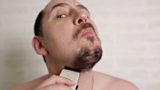 Un uomo rasa una grande barba con un rasoio elettrico. ritratto ravvicinato di una persona — Video Stock