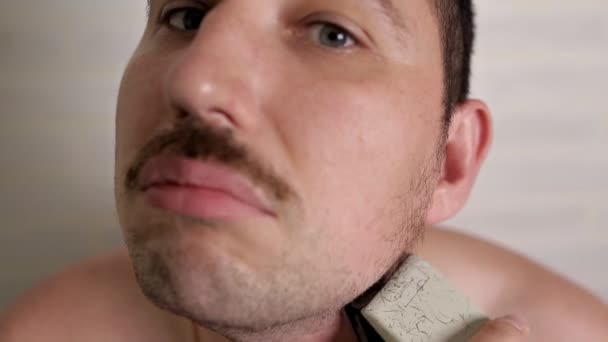 Un uomo rasa una grande barba con un rasoio elettrico. ritratto ravvicinato di una persona — Video Stock