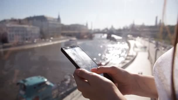 Mooi meisje met lang haar in zonnebrillen met smartphone app bij zonsondergang op de brug — Stockvideo