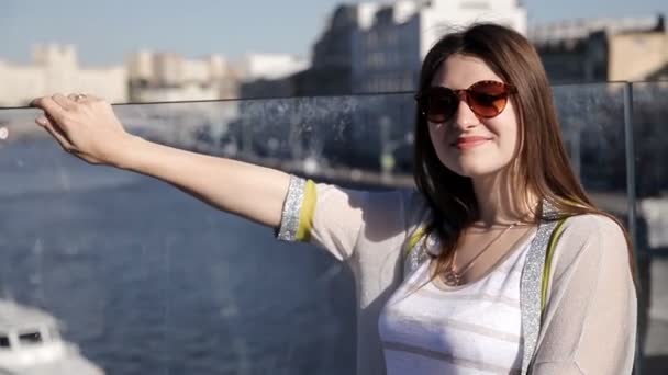 Junges lächelndes Model mit langen blonden Haaren posiert auf einer Brücke mit einem Haus am Fluss — Stockvideo