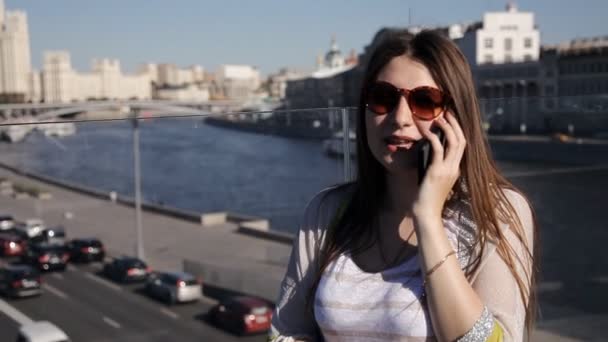 Beautiful attractive young woman standing on the bridge and uses a smartphone. Below is a stream of cars — Stock Video