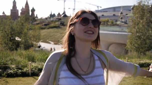 Młoda atrakcyjna kobieta jest chodzenie w parku na zielonym trawniku i uśmiechnięta-natura z nowoczesnymi budynkami — Wideo stockowe