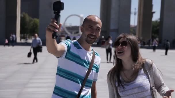 若いカップル、男と女が町の広場に沿って歩いて、カメラに自分自身を取っています。観光客、遠足、射撃 — ストック動画