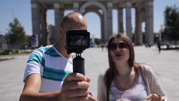 Um jovem casal, um homem e uma mulher estão andando pela praça da cidade e se filmando. Turistas, excursão, tiroteio — Vídeo de Stock