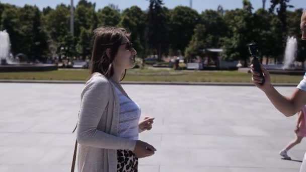 Een jonge kerel schiet een meisje op een videocamera, in het centrale plein van de stad, op het Europese plein. Journalist, rapportage, schieten — Stockvideo