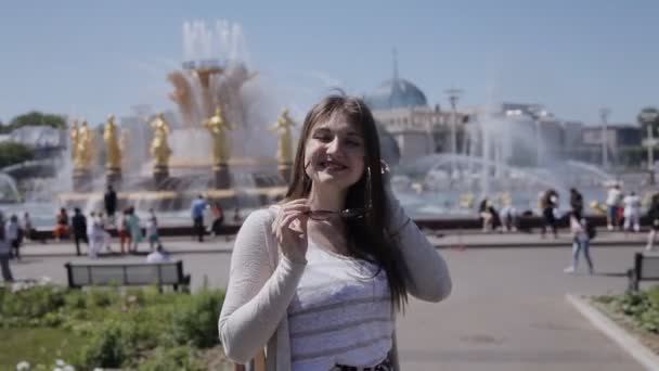 Молодая девушка в солнечных очках позирует перед камерой на фоне фонтана со статуями. Древний фонтан в Европе — стоковое видео