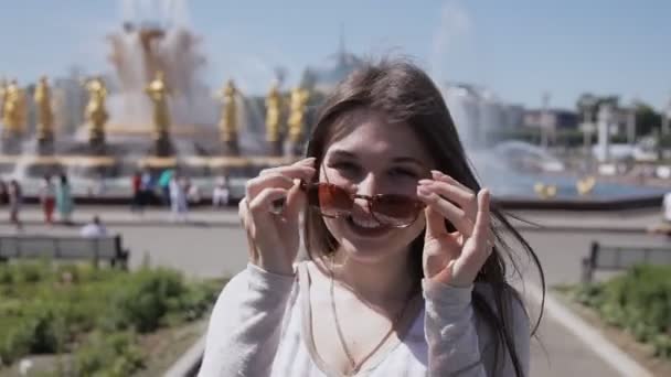 Młoda dziewczyna w okulary stwarzające w aparacie na tle fontanny z rzeźbami. Starożytna fontanna w Europie — Wideo stockowe