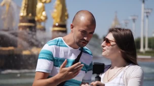 Молоді блогери чоловік і жінка знімають на камеру біля фонтану з золотими статуями. Європі — стокове відео