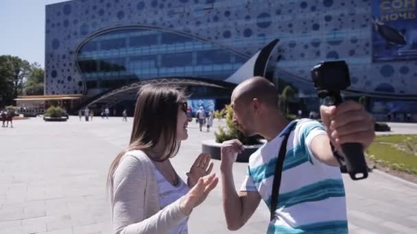 男性と女性のビデオブロガーは、都市の水族館の近くの都市の広場でカメラで自分自身の写真を撮ります — ストック動画