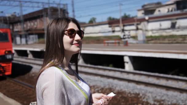 Une fille avec un billet à la main est debout sur le quai de la gare et attend le train. Approche train à la plate-forme — Video