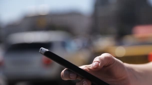 Una ragazza usa un telefono cellulare per strada in una giornata di sole sullo sfondo di un flusso di auto di passaggio . — Video Stock